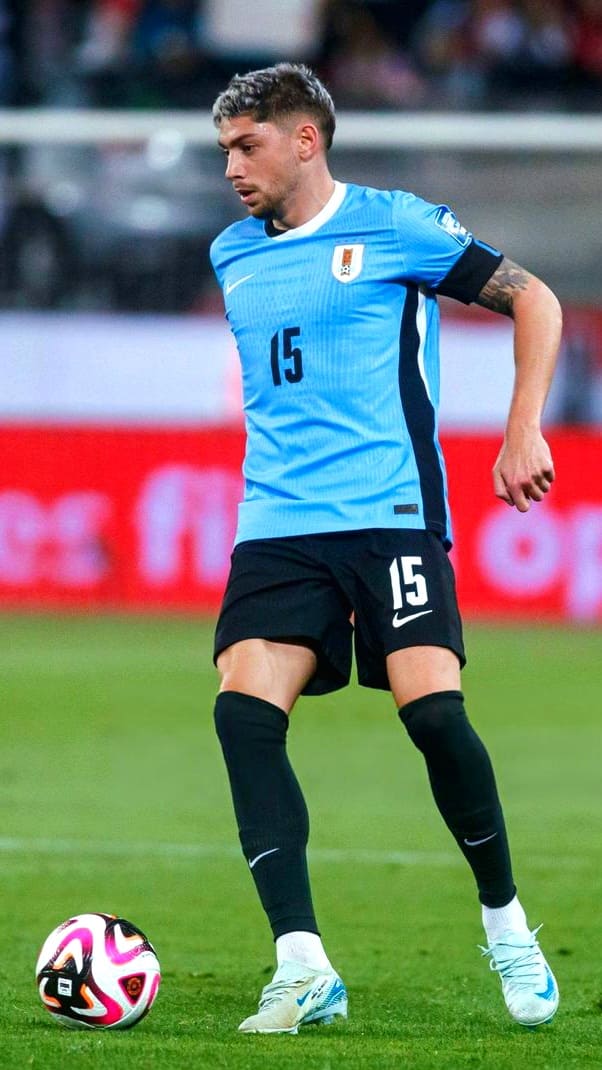 A soccer player in a light blue jersey with the number 15 controls the ball on the field during a match, sporting black shorts, black socks, and white cleats—catch all the action live with Romania IPTV.