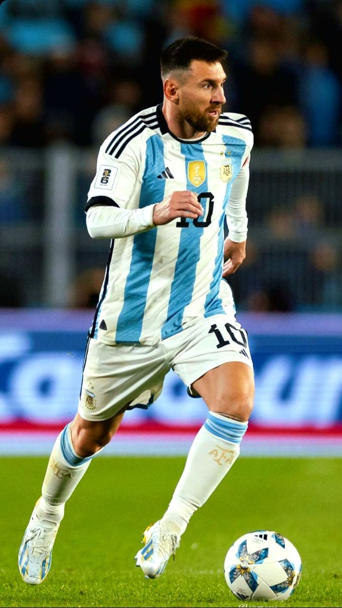A soccer player wearing Argentina's national team uniform, number 10, is running with the ball on the field during a match. The scene, perfect for Romania IPTV viewers, features blurred spectators and shining stadium lights in the background.